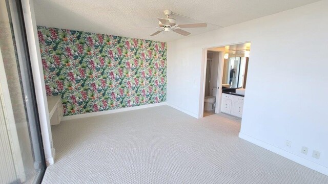 unfurnished bedroom featuring ceiling fan, light colored carpet, connected bathroom, and a textured ceiling