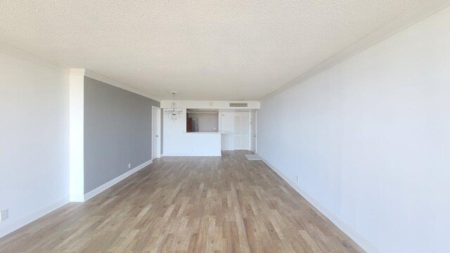 hall with a textured ceiling, crown molding, an inviting chandelier, and light wood-type flooring