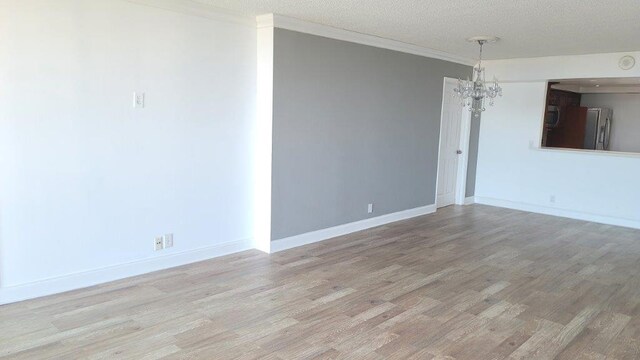 empty room featuring a textured ceiling, ornamental molding, light hardwood / wood-style floors, and a notable chandelier