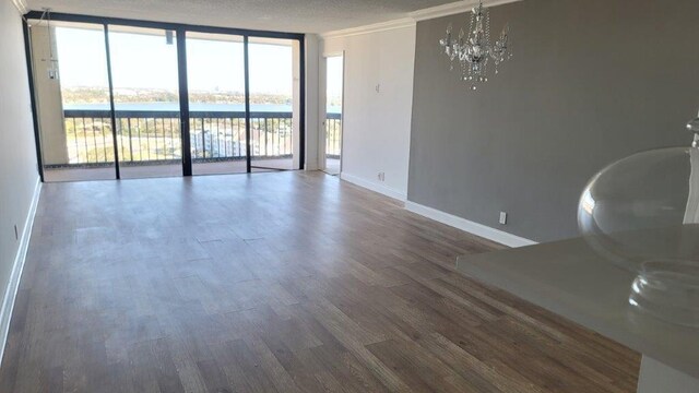 empty room featuring a wall of windows, dark hardwood / wood-style floors, a notable chandelier, a water view, and crown molding