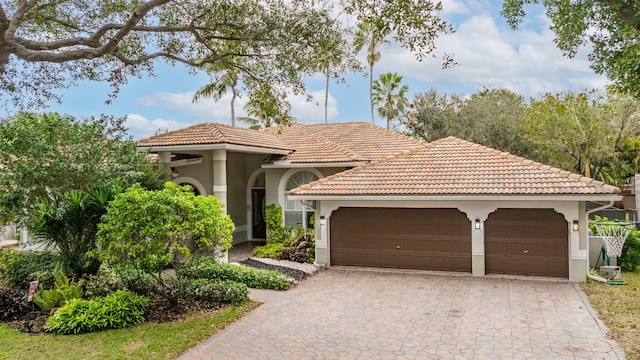 mediterranean / spanish-style house with a garage, decorative driveway, a tiled roof, and stucco siding