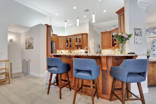 kitchen featuring light stone counters, a peninsula, visible vents, decorative backsplash, and brown cabinetry