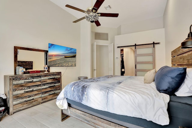 bedroom with a barn door, visible vents, a ceiling fan, wood finished floors, and vaulted ceiling