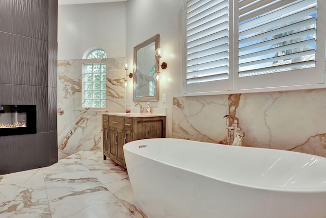 bathroom with a large fireplace, marble finish floor, a freestanding tub, and vanity