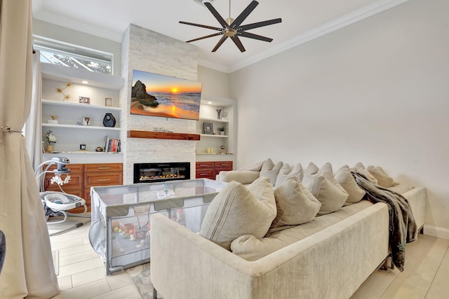 living area with built in shelves, a fireplace, ornamental molding, a ceiling fan, and baseboards