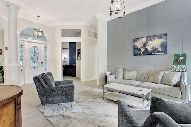 living area with crown molding, a decorative wall, a chandelier, light wood-type flooring, and ornate columns