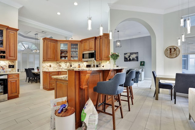 kitchen featuring ornamental molding, stainless steel microwave, brown cabinetry, and tasteful backsplash