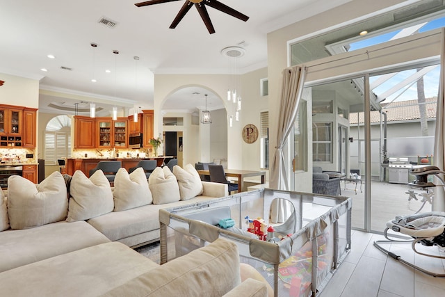 living area featuring ceiling fan, visible vents, arched walkways, and crown molding