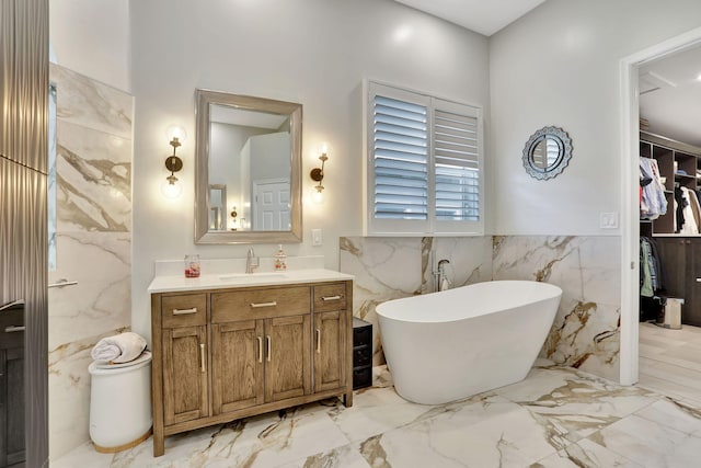 bathroom featuring marble finish floor, tile walls, a freestanding bath, a spacious closet, and vanity