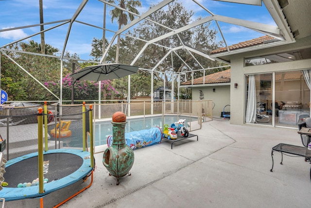 view of swimming pool featuring glass enclosure, a trampoline, a patio area, and a fenced in pool