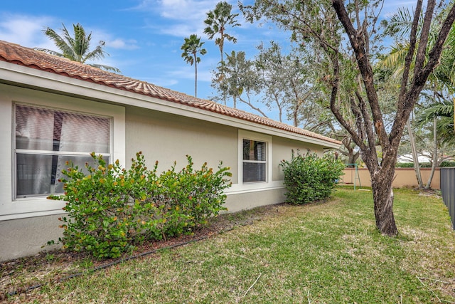 view of property exterior featuring stucco siding, a tile roof, fence, and a yard