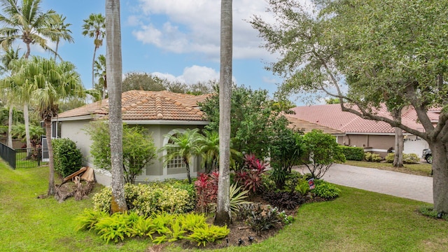 view of side of property featuring decorative driveway, stucco siding, a lawn, fence, and a tiled roof