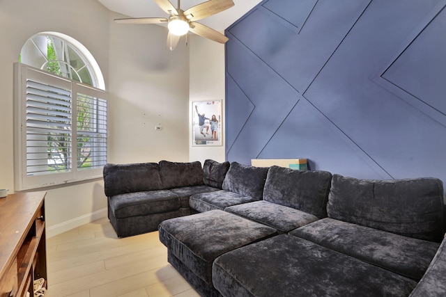 living room featuring a towering ceiling, wood finished floors, a ceiling fan, and baseboards