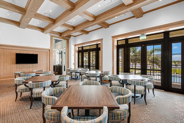 carpeted dining space featuring a towering ceiling, french doors, coffered ceiling, and wooden walls