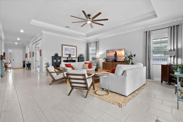 living room featuring ceiling fan, ornamental molding, and a tray ceiling