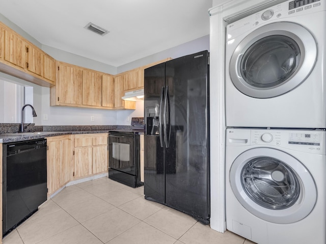 kitchen with light brown cabinets, light tile patterned floors, black appliances, and stacked washer / drying machine