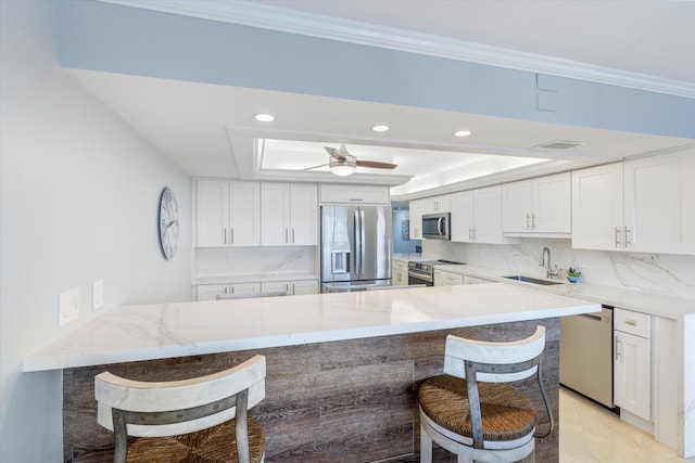 kitchen with stainless steel appliances, white cabinets, a raised ceiling, kitchen peninsula, and a breakfast bar area