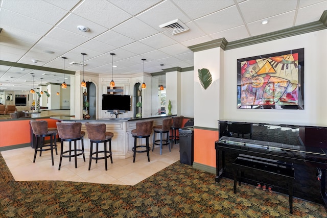 kitchen featuring a breakfast bar area, hanging light fixtures, kitchen peninsula, ornamental molding, and a drop ceiling