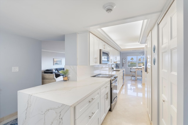 kitchen featuring appliances with stainless steel finishes, white cabinetry, light stone countertops, and sink