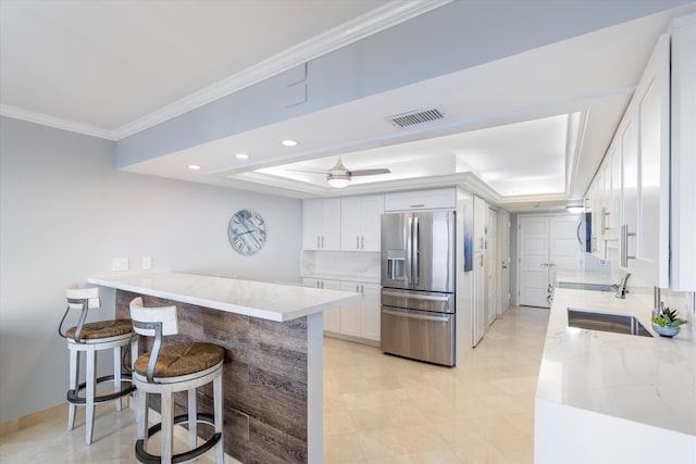 kitchen with kitchen peninsula, stainless steel fridge, a tray ceiling, sink, and white cabinetry