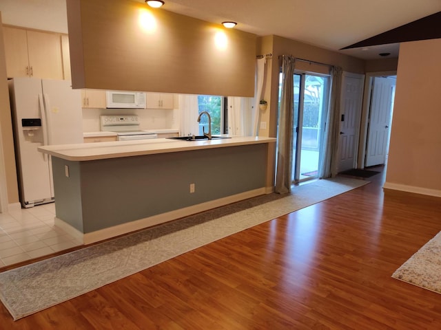 kitchen featuring vaulted ceiling, sink, kitchen peninsula, white appliances, and light hardwood / wood-style flooring