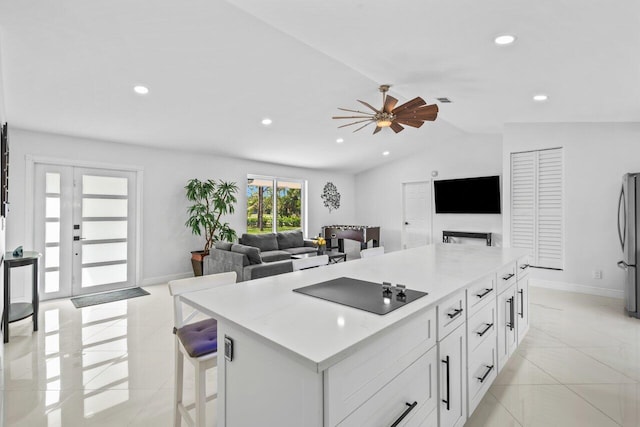 kitchen with lofted ceiling, ceiling fan, stainless steel fridge, black electric cooktop, and white cabinetry