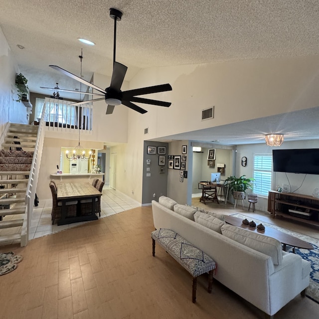 living room featuring a textured ceiling, light hardwood / wood-style floors, high vaulted ceiling, and ceiling fan with notable chandelier