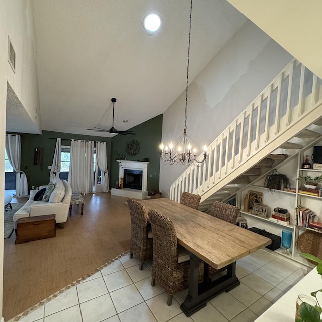 tiled dining area featuring ceiling fan with notable chandelier and high vaulted ceiling