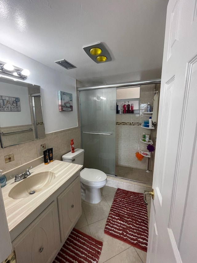 bathroom featuring tile patterned floors, toilet, vanity, a shower with shower door, and tile walls