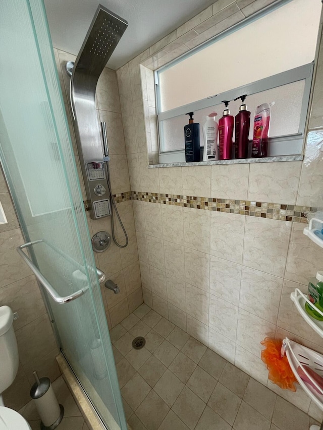 bathroom with tile patterned flooring, toilet, a shower with door, and tile walls