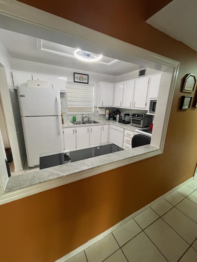 kitchen with sink, light tile patterned floors, kitchen peninsula, white fridge, and white cabinets