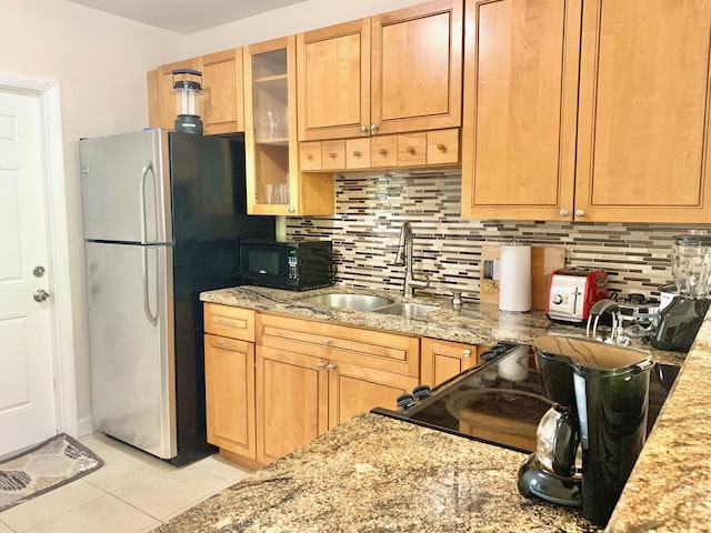 kitchen featuring tasteful backsplash, sink, light tile patterned floors, stainless steel fridge, and light stone counters