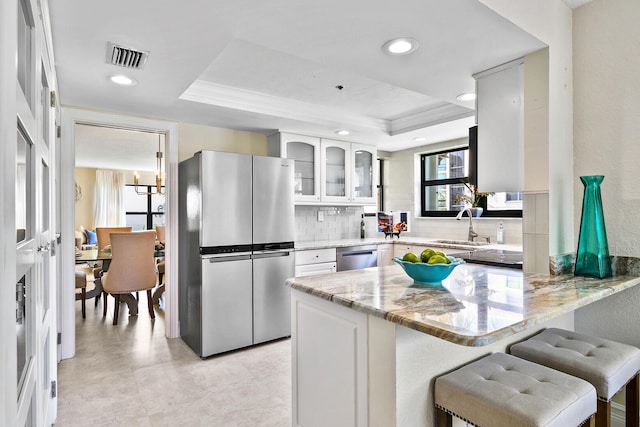 kitchen featuring stainless steel appliances, kitchen peninsula, light stone countertops, and a tray ceiling