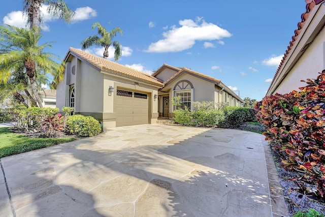 mediterranean / spanish house with a tile roof, a garage, driveway, and stucco siding