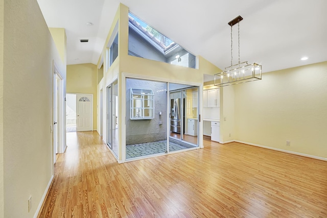 interior space with high vaulted ceiling, light hardwood / wood-style floors, and a skylight