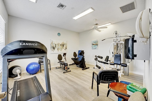 workout room with ceiling fan, light hardwood / wood-style flooring, and a textured ceiling