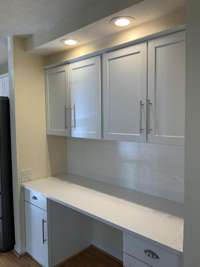 kitchen featuring white cabinetry, wood-type flooring, built in desk, stainless steel fridge, and decorative backsplash