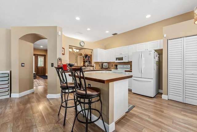 kitchen featuring white cabinets, white appliances, a kitchen breakfast bar, kitchen peninsula, and butcher block countertops