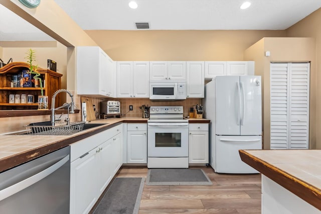 kitchen featuring white appliances, tile countertops, light wood-type flooring, white cabinets, and sink