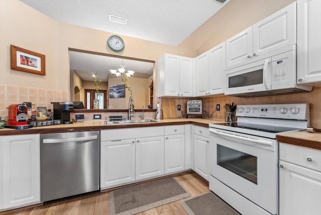 kitchen with white appliances, white cabinets, a chandelier, and sink