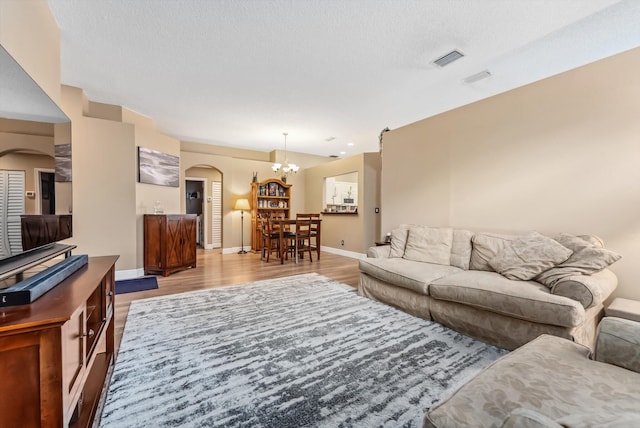 living room with light hardwood / wood-style floors, an inviting chandelier, and a textured ceiling