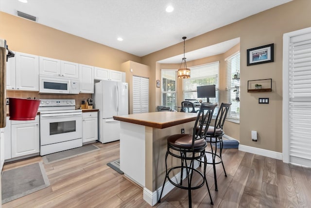 kitchen featuring white appliances, light wood-type flooring, a notable chandelier, pendant lighting, and white cabinets