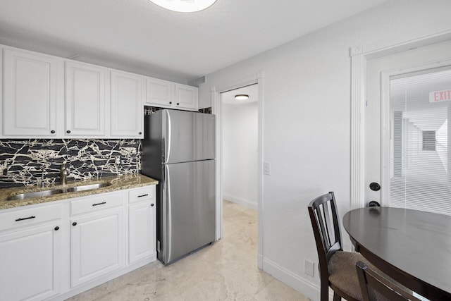 kitchen featuring white cabinetry, tasteful backsplash, sink, stainless steel fridge, and light stone counters