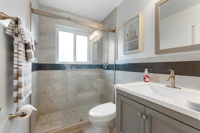 bathroom with tile walls, a shower with shower door, vanity, and toilet