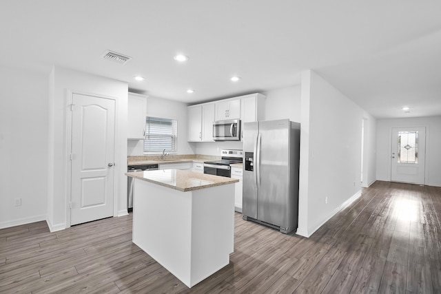 kitchen featuring a kitchen island, white cabinetry, light stone counters, stainless steel appliances, and light wood-type flooring