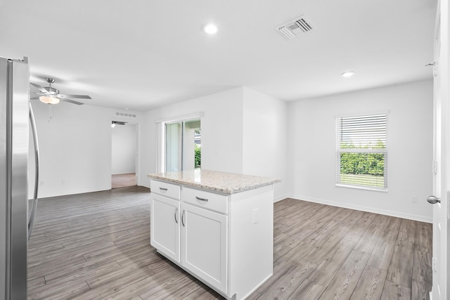 kitchen with light hardwood / wood-style flooring, stainless steel refrigerator, white cabinetry, light stone counters, and a kitchen island