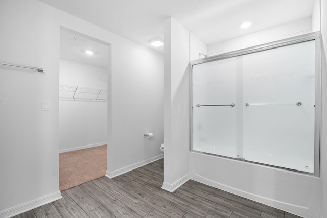 bathroom featuring hardwood / wood-style flooring, enclosed tub / shower combo, and toilet