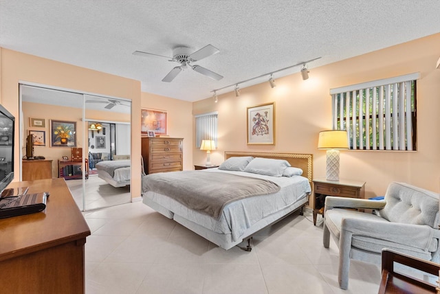 tiled bedroom featuring track lighting, a closet, ceiling fan, and a textured ceiling