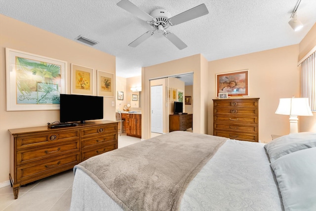 tiled bedroom with ceiling fan, a closet, a textured ceiling, and rail lighting