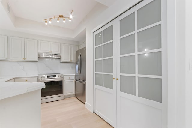 kitchen featuring appliances with stainless steel finishes, tasteful backsplash, white cabinets, light stone countertops, and light wood-type flooring